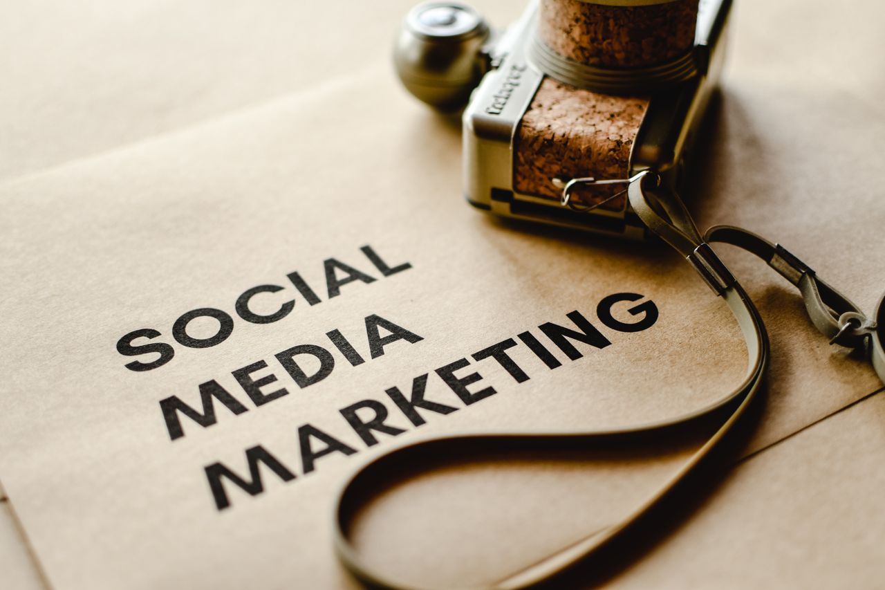 heros-img Close-up of a camera placed on brown paper with Social Media Marketing text, emphasizing digital marketing themes.
